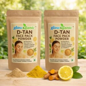 Two pouches of glow&ganic D-TAN Face Pack Powder displayed with raw turmeric root, sliced lemon, and natural powders